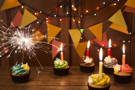 Chocolate cupcakes with colourful icing and candles against festive background with garland. Card mockup, copy space. Birthday, party, holiday conceptの写真素材