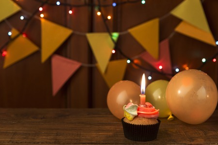 Chocolate cupcake with colourful icing and candle against festive background with garland and...
