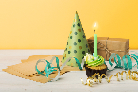 Delicious cupcake with candle , gift and dotted cap on yellow background, copy space. Birthday, party, holiday conceptの写真素材