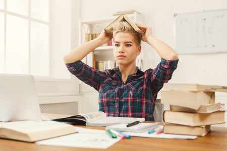 Tired girl studying at working table. Exhausted female student reading books and working on laptop. Education and technology conceptの写真素材