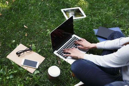 Young unrecognizable woman sitting outdoors on grass with laptop, typing, surfing internet, preparing for exams. Technology, communication, education and remote working concept, copy spaceの写真素材