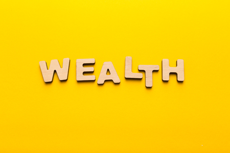Wealth word inscription made of wooden letters on yellow background. Financial health and economics concept, top view, copy spaceの写真素材
