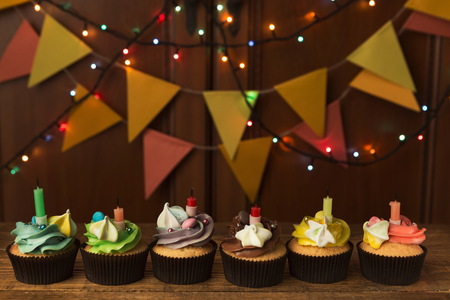 Chocolate cupcakes with colourful icing and candles against festive background with garland. Card mockup, copy space. Birthday, party, holiday conceptの写真素材