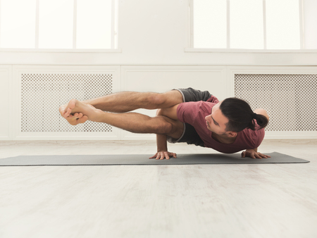 Young strong man practicing yoga, standing in flexible pose on hands on mat in fitness class, making balance exercise, copy spaceの写真素材