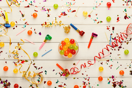 Birthday party background. Top view on holiday decorations, confetti, candles and candies bowl on white wooden planks. Celebration conceptの写真素材