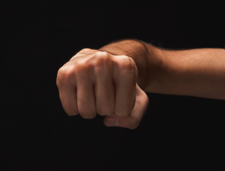 Male hand clenched fist on black isolated background, low key, cutout. Strenght and agression conceptの写真素材