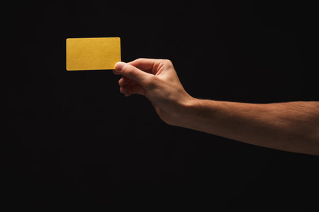 Male hand holding blank plastic credit card or business card on black isolated studio background. Banking services and acquaintance concept, copy space, cutout, low keyの写真素材