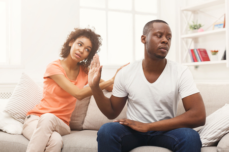 Young african-american couple making peace after quarreling at home, man still feeling offended. Family relationship difficulties concept, copy spaceの写真素材
