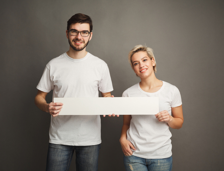 Happy young couple holding blank white banner with copy space on gray backgroundの写真素材