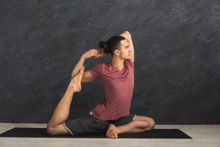 Young strong man practicing yoga, standing in flexible pose on mat in fitness class, making asana exercise, copy spaceの写真素材