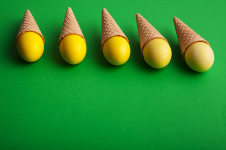 Easter background. Yellow colored eggs in waffle cones on green surface. Minimalistic design of greeting card, mockup, copy space, flat layの写真素材