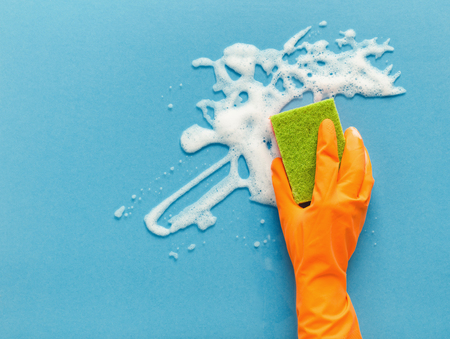 Cleaning concept - hand in orange protective rubber glove washing glass window with sponge and detergent foam. Householding background, copy spaceの写真素材