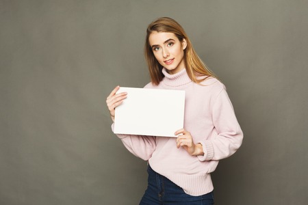 Young woman with blank white paper. Attractive smiling girl holding advertising sheet, copy spaceの写真素材