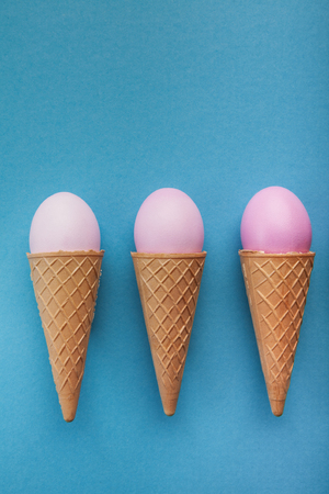 Easter background. Pink colored eggs in waffle cones on blue surface. Minimalistic design of greeting card, mockup, top view, copy space, flat lay, top viewの写真素材