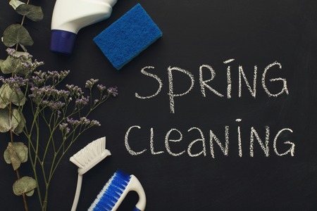 Spring cleaning background. Assortment of colorful spray detergents, sponges, rags and other supplies on black board with chalk inscription. Cleaning services and tidying up concept, top viewの写真素材