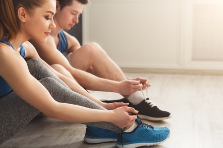Couple tying up laces on sport shoes closeup. Sporty man and woman preparing for training, wearing...