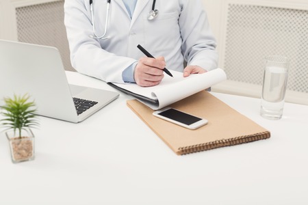 Unrecognizable male doctor writing notes in clipboard while working at her office. Always ready to help, medicine concept, copy spaceの写真素材