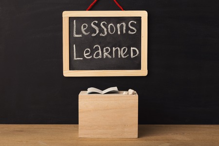Word lessons learned written on miniature chalkboard in classroom against black background. Back to...