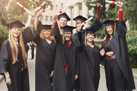 A group of multietnic graduate students celebrating by holding their diploma. Education, qualification and gown concept.の写真素材