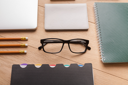 Glasses, pencils and notepads on office wooden desk, above view. Geometrical workplace, lifestyle concept.の写真素材