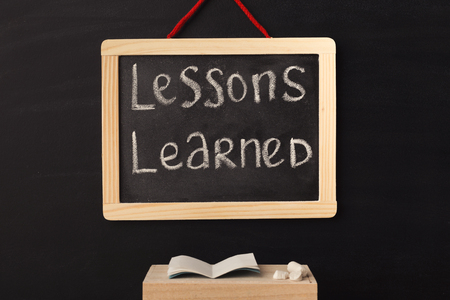 Word lessons learned written on miniature chalkboard in classroom against black background. Back to school concept. Educational background.の写真素材