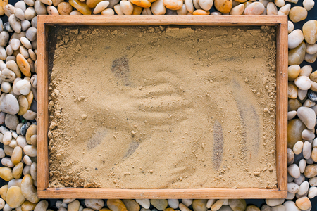 Wooden tray with beach sand on sea pebbles background, top view. Copy space for text, advertisement or drawing. Travelling and summer vacation conceptの写真素材