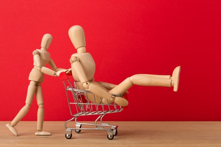Wooden mannequins with miniature shopping cart running for sales on red background. Mockup for...