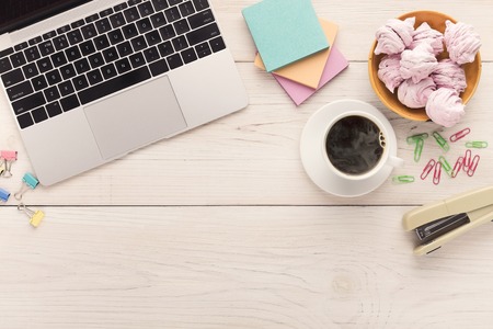 Desk with coffe cup, laptop keyboard, sweets and stationery on white background, copy space, top...