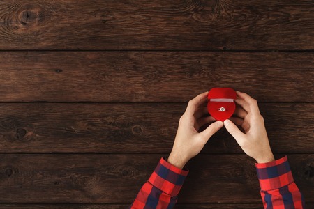 Top view on male hands with proposal ring on brown wooden background. Man prepare for proposal to marry him. Valentine, happiness, relationships, love, engagement concept, copy spaceの写真素材