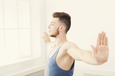 Man training yoga pose in gym at white background, copy space. Young boy makes exercise, fitness,...