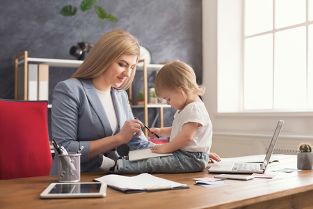Happy beautiful business mom working on laptop and taking notes while spending time with her cute baby. Business, motherhood, multitasking and family concept.の写真素材