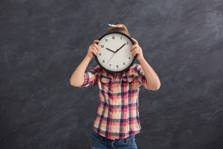 Little girl holding big clock, covering her face. Time management, deadline, time to study, school...