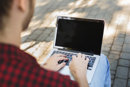 Male hands with laptop closeup, over shoulder shot. Man working outdoors on computer with blank...