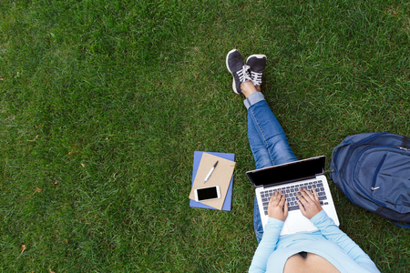 Top view of woman sitting in park on the green grass with laptop, notebook, backpack and smartphone, hands on keyboard. Copy spaceの写真素材