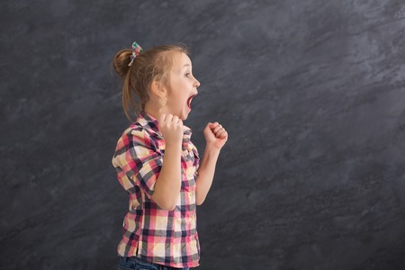 Feeling happy. Excited little girl gesturing with raised arms on gray studio background, copy spaceの写真素材