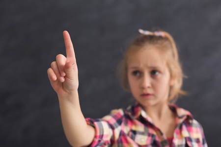 Serious little girl pointing on virtual object with finger at black studio background, copy spaceの写真素材
