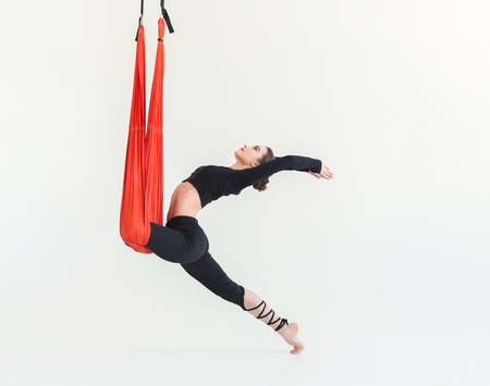 Young slim woman practicing fly yoga warrior asana over white background in fitness studio, copy space. Health, sport, yoga conceptの写真素材