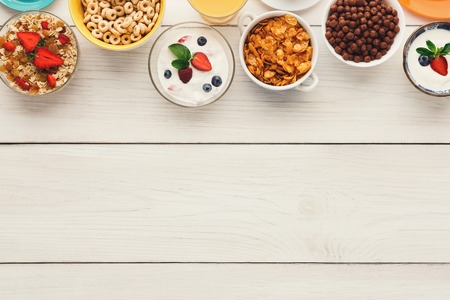 Healthy breakfast meals on wooden table copy space. Muesli, cornflakes, chocolate cereal balls and yogurt with berries frame, top viewの写真素材
