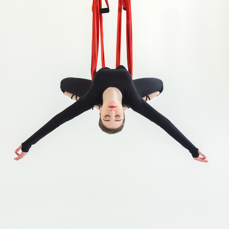 Young slim woman practicing fly yoga asana over white background in fitness studio, copy space, crop. Health, sport, yoga conceptの写真素材