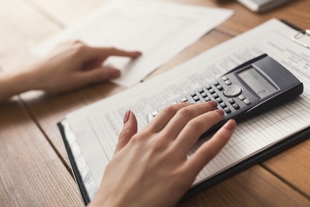 Closeup of woman hands counting on calculator and reading documents. Financial background, count and pay an account, copy spaceの写真素材