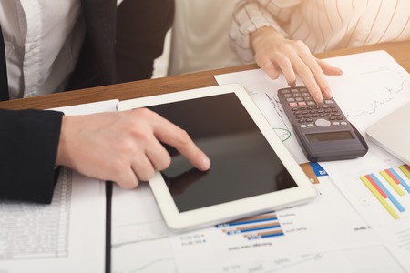 Closeup of business colleagues hands counting on calculator and using digital tablet with blank screen for advertisement. Financial background, count and pay an account, copy spaceの写真素材