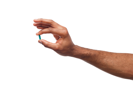 Black male hand holding a pill between thumb and forefinger isolated on white background. Health care, treatment conceptの写真素材