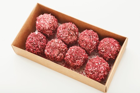 Raw vegan candies in red coconut flakes in craft box isolated on white background. Healthy dessert...