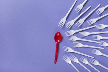 Red spoon against lots of white plasic forks on purple background with copy space, top view. Opposition, be brave and different, leadership conceptの写真素材