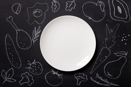 Hand drawn food on chalkboard and empty white plate, top view. Mockup for restaurant menu with copy space on platterの写真素材
