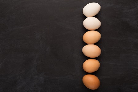 Gradient of natural colored eggs arranged in a row on black background. Minimalistic Easter greeting card or organic meals advertizing, top view, copy spaceの写真素材