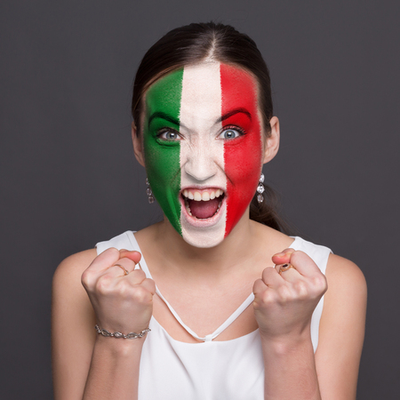 Portrait of happy woman with the flag of Italy painted on his face. Football or soccer team fan, sport event, faceart and patriotism concept. Studio shot at gray background, copy spaceの写真素材