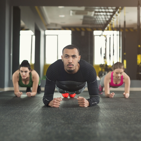 Fitness group doing plank workout training with coach indoors. Young men and women making exercise at gym. Healthy lifestyle, gymnastics concept, copy spaceの写真素材
