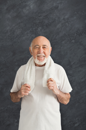 Cheerful senior man in sportswear relax after training, standing with towel on shoulders, black background. Active lifestyle and healthcare in any age, copy spaceの写真素材
