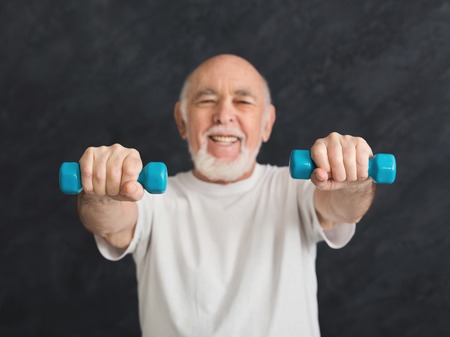 Senior fitness man training with dumbbells at gym, doing strength exercise for biceps, black background. Active lifestyle and healthcare in any age, copy spaceの写真素材